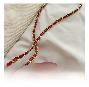 Détail d'un sac de mariée rouge avec une chaîne tissée en métal doré et cuir