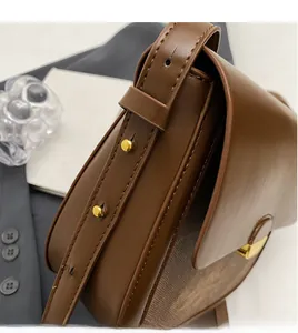Détail de la bandoulière en cuir marron et des boucles dorées du sac besace