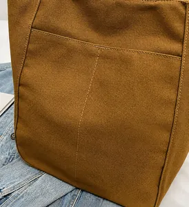 Detalle de la textura del bolso de lona marrón con costuras finas y bolsillo exterior