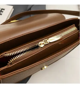 Détail de la fermeture dorée et doublure en tissu rouge sur un sac en cuir marron foncé