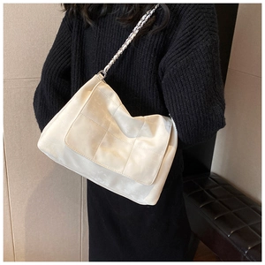 Detail of white quilted faux leather bag with silver chain strap worn by a model