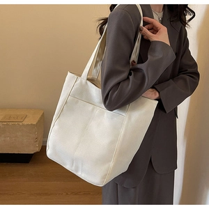 Modelo luciendo un gran bolso tote de lona blanca con bolsillo frontal para diario