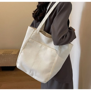 Detalle del bolso tote de lona blanco roto con textura gruesa y bolsillo frontal al hombro