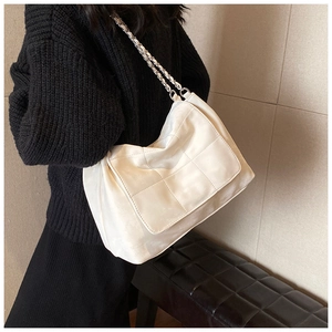 Detail of white quilted tote bag with silver chain strap shown on a model for commute