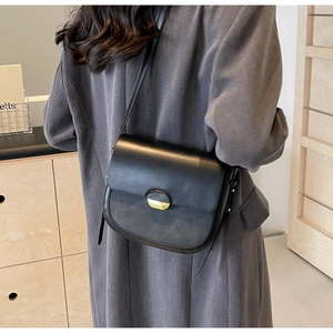 Détail du sac besace en cuir noir mat avec boucle dorée sur un blazer en laine gris foncé