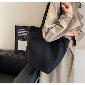 Detalle de un bolso tote grande de lona negra combinado con una gabardina color caqui