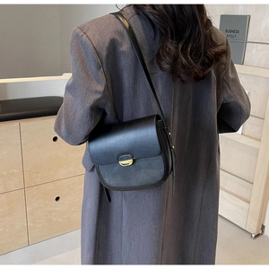 Vue latérale d'un sac besace noir avec boucle dorée porté par un mannequin à l'épaule
