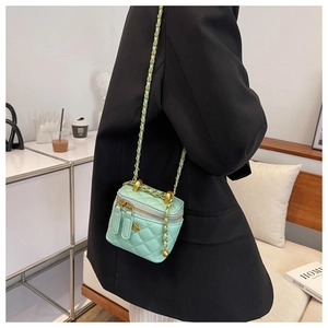 Detail of mint green quilted mini vanity bag with gold chain strap and floral charm accessory