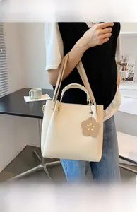 Detail of cream-white tote bag with gold hardware and a floral leather charm accessory