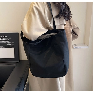 Detalle de bolsa tote grande de lona negra llevada por modelo en un estudio minimalista
