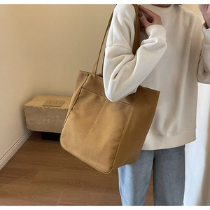 Vista detallada de un bolso tote de lona marrón con triple costura llevado por una modelo