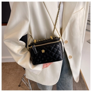Close-up of black quilted chain bag with a gold flower emblem on white blazer