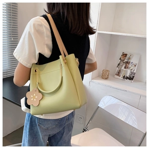Detail view of a green tote bag featuring light brown straps and a pink flower charm