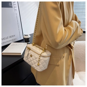 Detail of white quilted bucket bag with gold camellia logo and chain strap on model