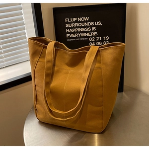 Detalle de un bolso tote de lona amarillo mostaza con pespuntes en una mesa de metal