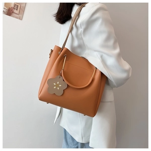 Detailed side view of orange-brown tote bag with flower charm and golden hardware