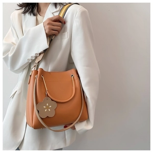 Detail of warm orange bucket bag with stylish wide woven strap and floral charm accessory