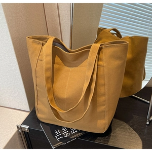 Detalle del bolso tote de lona amarillo mostaza con correas gruesas y bolsillo frontal