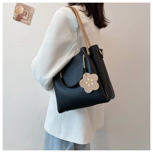 Detail of black tote bag with golden metal handle and brown flower charm accessory