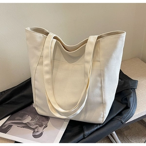 Detalle del bolso tote grande de lona crema con correa ancha y bolsillo delantero