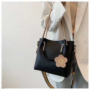 Detail of black tote bag with gold metal handles and striped shoulder strap on a model