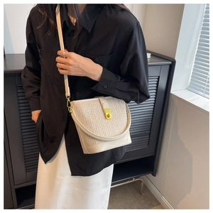 Detail view of woven bucket bag with gold clasp and leather shoulder strap worn by model