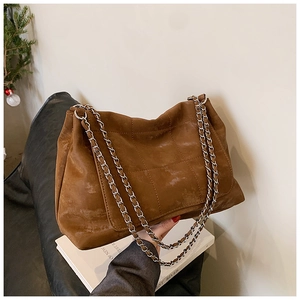 Detail of a brown suede tote bag with quilted stitching and a silver chain shoulder strap