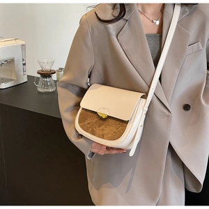 Détail d'un sac besace bicolore crème et marron porté sur un blazer de couleur kaki
