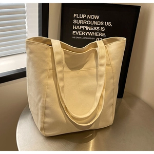 Bolso tote de lona color crema con bolsillo frontal espacioso sobre una mesa de metal