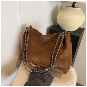 Detail of caramel brown quilted tote bag with silver chain strap on minimalist display