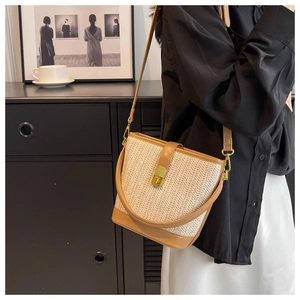 Detail of cream woven bucket bag with brown leather trim and gold metal clasp closure
