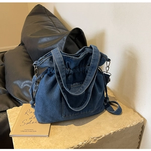Detail view of dark blue denim bucket bag with drawstring closure and stone pedestal base