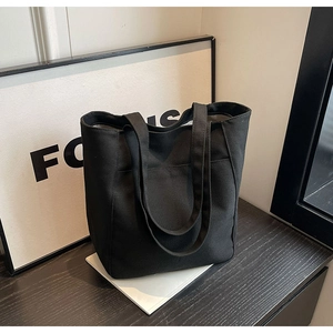 Detalle de bolso tote de lona negra minimalista con práctico bolsillo frontal antirrobo