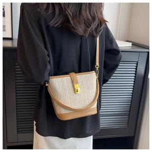 Close-up of woven straw bucket bag with brown leather details and golden swivel lock