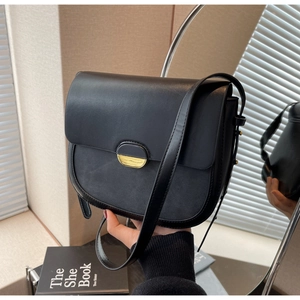 Détail d'un sac besace noir avec boucle dorée ovale et bandoulière en cuir souple