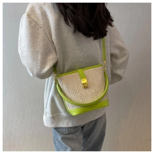 Detail of woven straw bucket bag with neon green leather trim shown as a crossbody