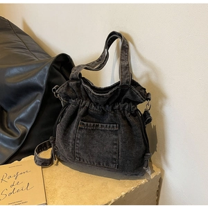Detail of washed black denim bucket bag featuring drawstring closure and front pocket