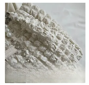 Macro detail of creamy white bubble textured fabric with pearl and floral metal chain links