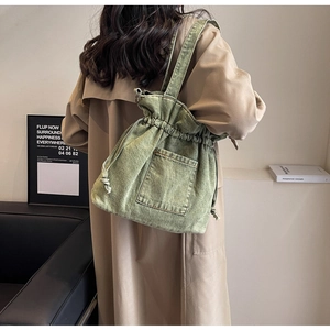 Lifestyle shot of green washed denim drawstring tote bag worn over a beige trench coat
