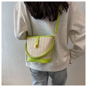 Detail of woven straw bucket bag with neon green leather trim shown on model