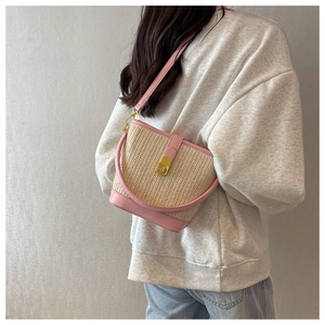 Detail of woven straw bucket bag with pink leather trim and gold metal lock buckle
