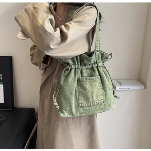 Washed green denim tote bag with drawstring closure worn as a crossbody by a model