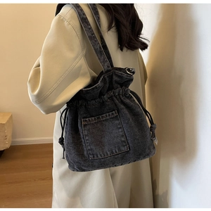 Detail of dark denim drawstring bucket bag with contrast stitching and shoulder strap