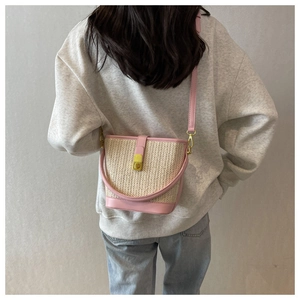 Close-up of woven straw bucket bag with pink leather trim and golden metal lock