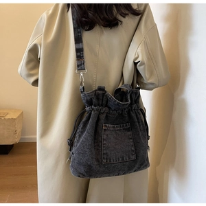 Detail of dark grey washed denim bucket bag with drawstring and silver hardware