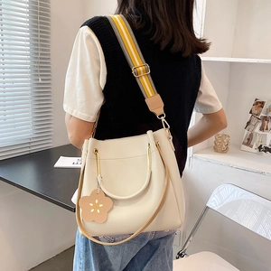 Cream bucket bag with striped strap and flower charm shown on person in bright interior