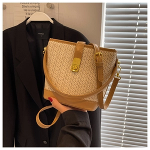 Detailed view of woven straw bucket bag with brown leather trim and golden metal lock