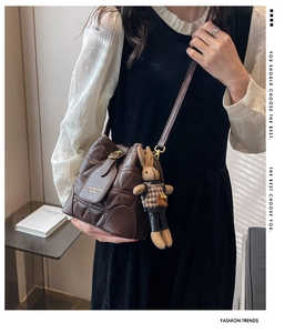 Detail of a brown quilted leather bucket bag with a cute knitted rabbit pendant charm