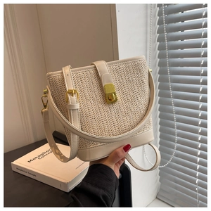 Detail of cream woven straw bucket bag with gold lock and leather trim in sunlight