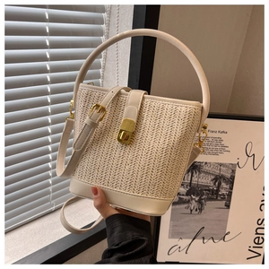 Detail of cream woven straw bucket bag showing leather stitching and gold twist lock